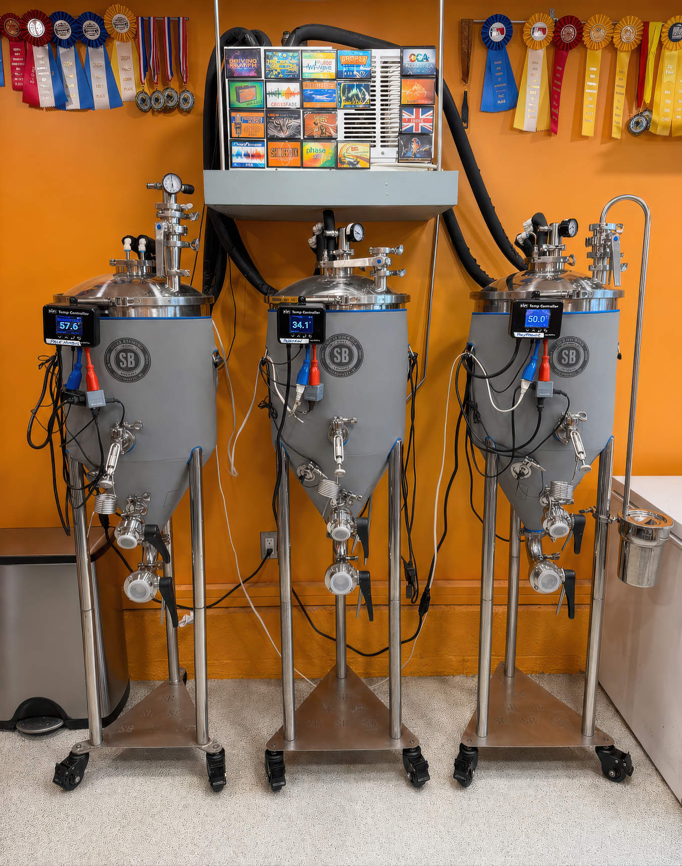 Three stainless fermenters against an orange brewery wall